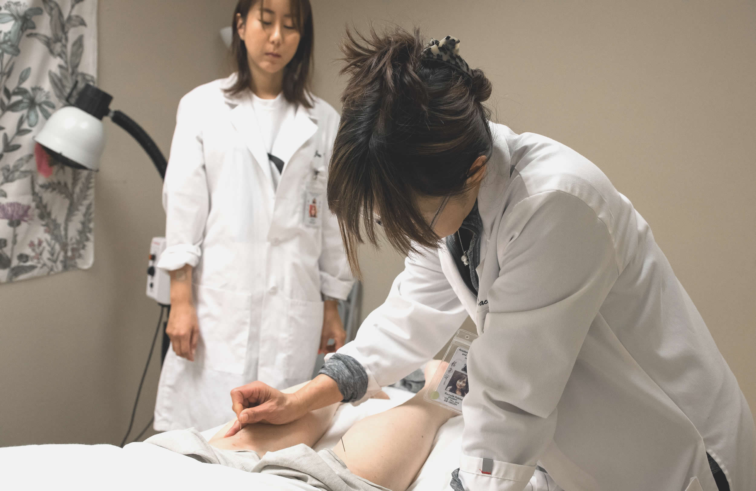 woman in lab coat practicing acupuncture being observed by practitioner