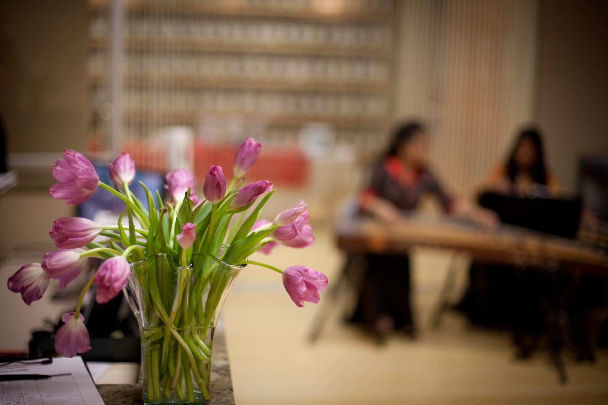 tulips in vase in foreground, woman at table talking in background